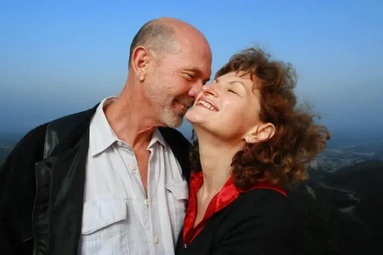 Older couple cuddling outdoors with the sea behind them