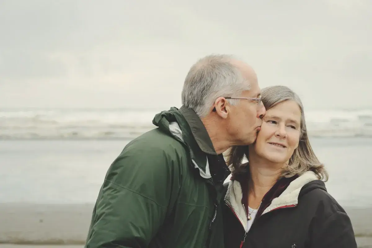 Man kissing woman on check beside body of water