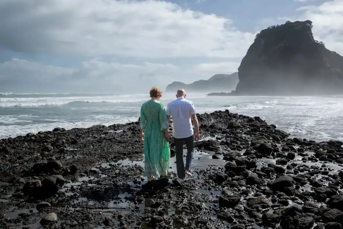 Tarisha and Mark walking hand in hand towards Lion Rock at Piha