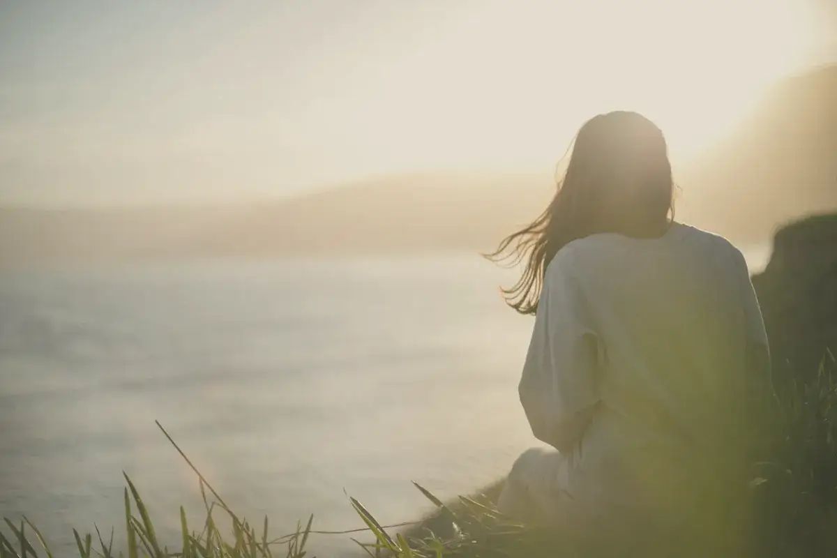 Woman wearing gray long-sleeved shirt facing the sea