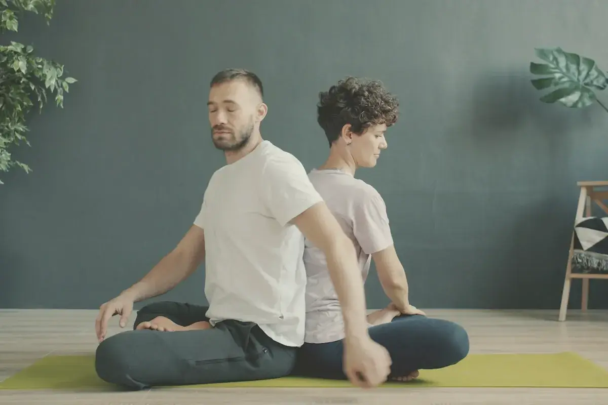 Two people meditating back to back on yoga mats