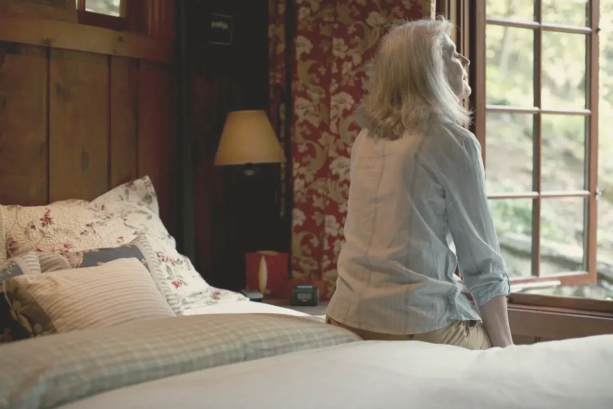Woman sitting on the edge of a bed looking out of the window
