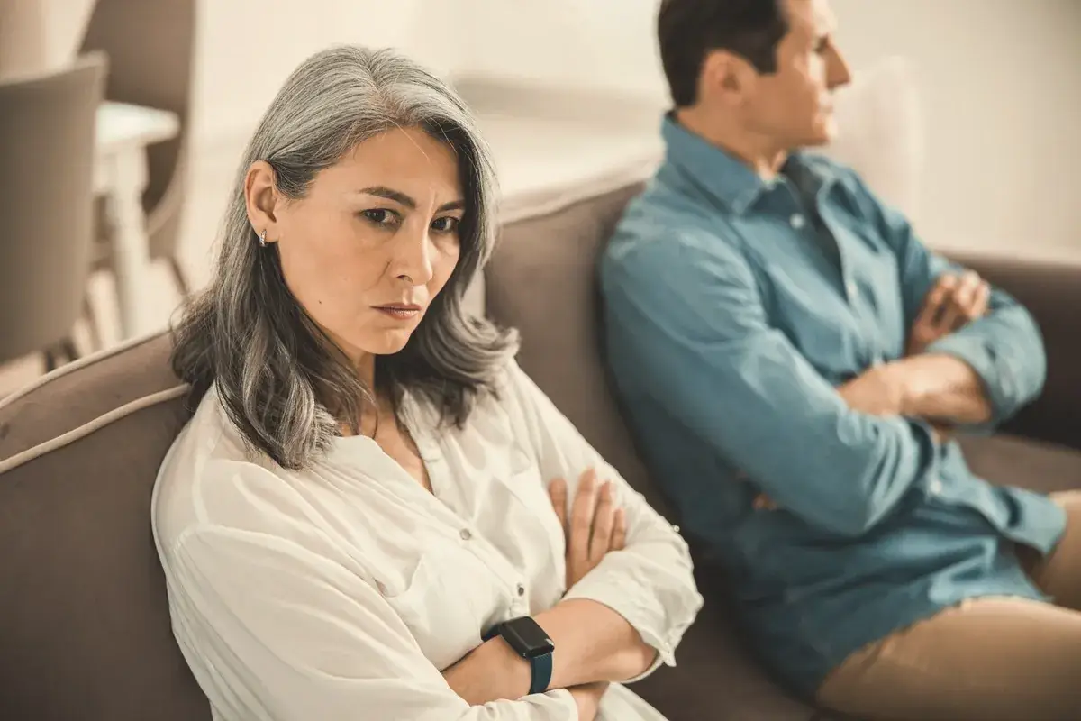 Couple sitting apart on a sofa with their arms folded